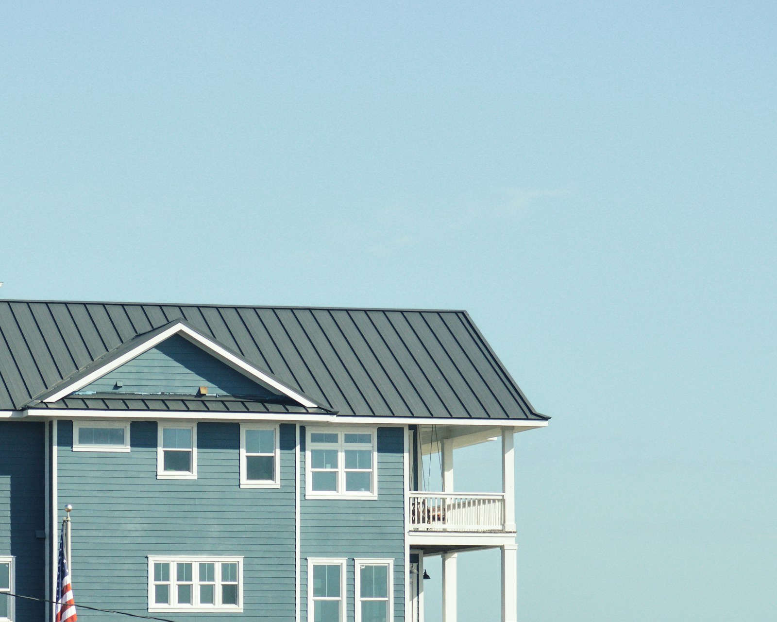 Finished blue house with a gray metal roof, white-trimmed windows and a covered upper porch.